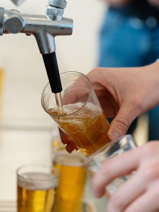 Nahaufnahme einer Person, die an einem Zapfhahn Bier in ein Glas füllt.