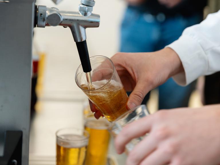 Nahaufnahme einer Person, die an einem Zapfhahn Bier in ein Glas füllt.