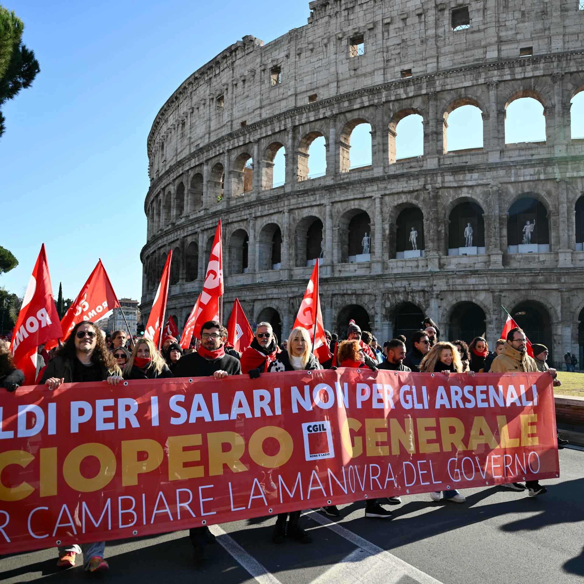 Nahe dem Kolosseum in Rom haben sich Menschen, die Fahnen tragen, hinter einem Banner versammelt. 