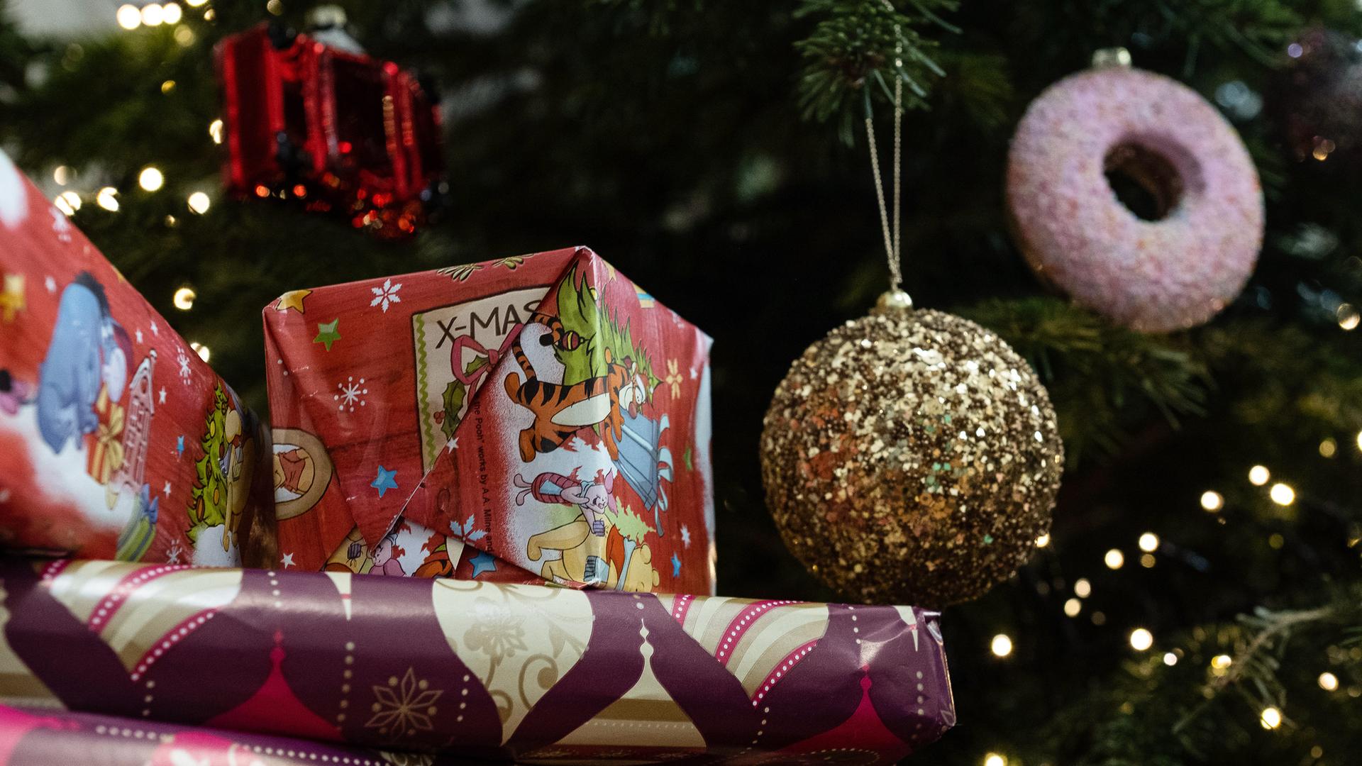 Eingepackte Geschenke liegen unter einem geschmückten Weihnachtsbaum. 