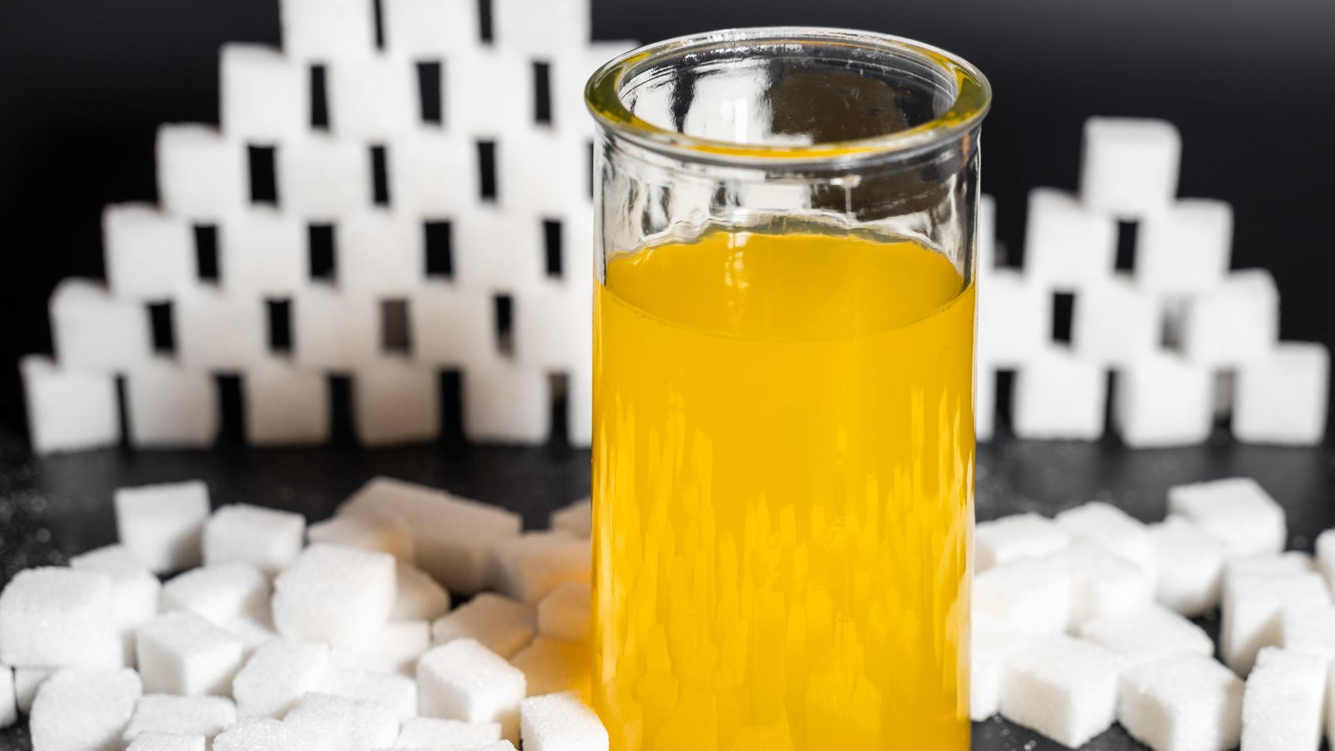 Glas mit gelber Limonade, umgeben von Würfel-Zucker. 