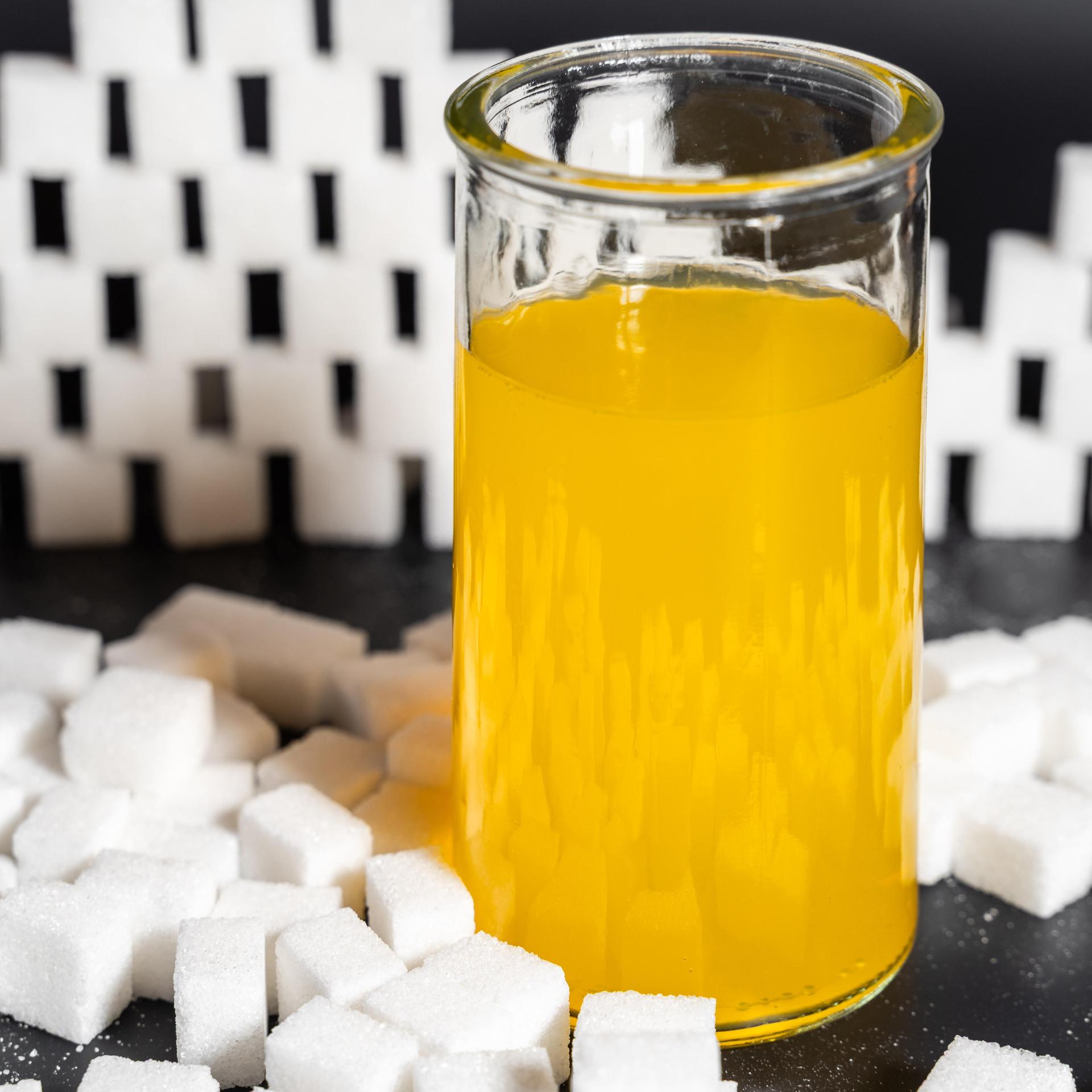 Glas mit gelber Limonade, umgeben von Würfelzucker. 