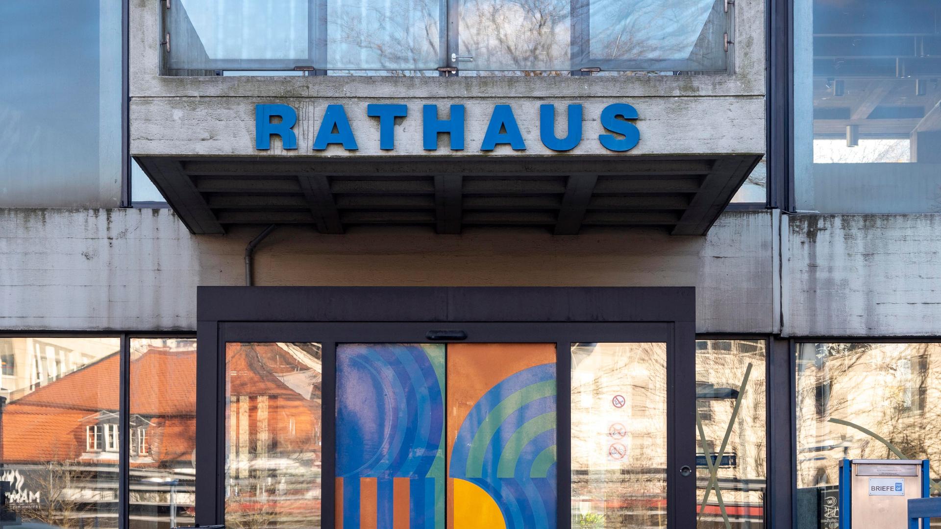Der Eingang zum Rathaus von Offenbach am Main. Es handelt sich um ein brutalistisches Gebäude aus Beton und Glas mit blauen Ornamenten auf der Eingangstür.