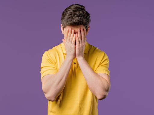 Ein weinender Mann, er trägt ein gelbes Poloshirt und hält die Hände vor den Kopf (Symbolbild)