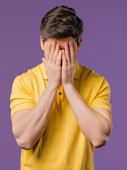 Ein weinender Mann, er trägt ein gelbes Poloshirt und hält die Hände vor den Kopf (Symbolbild)