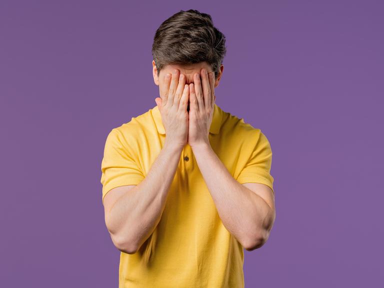 Ein weinender Mann, er trägt ein gelbes Poloshirt und hält die Hände vor den Kopf (Symbolbild)