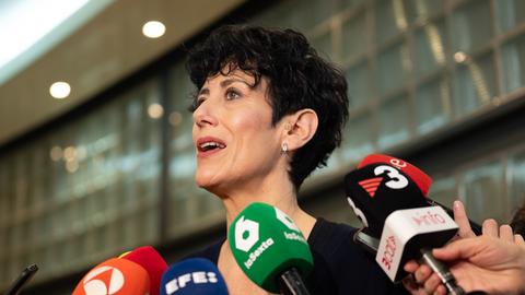 Elma Saiz steht zwischen Mikrofonen, umringt von Journalisten.