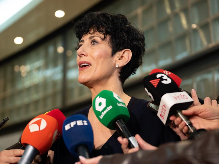 Elma Saiz steht zwischen Mikrofonen, umringt von Journalisten.