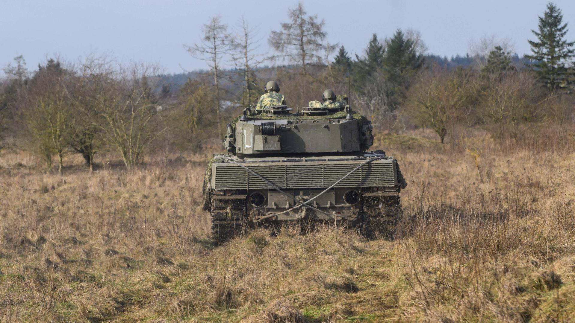 Zwei Soldaten fahren einen Panzer vom Typ Leopard durch eine Landschaft mit Bäumen.
