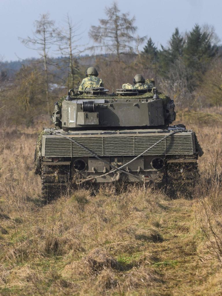 Zwei Soldaten fahren einen Panzer vom Typ Leopard durch eine Landschaft mit Bäumen.