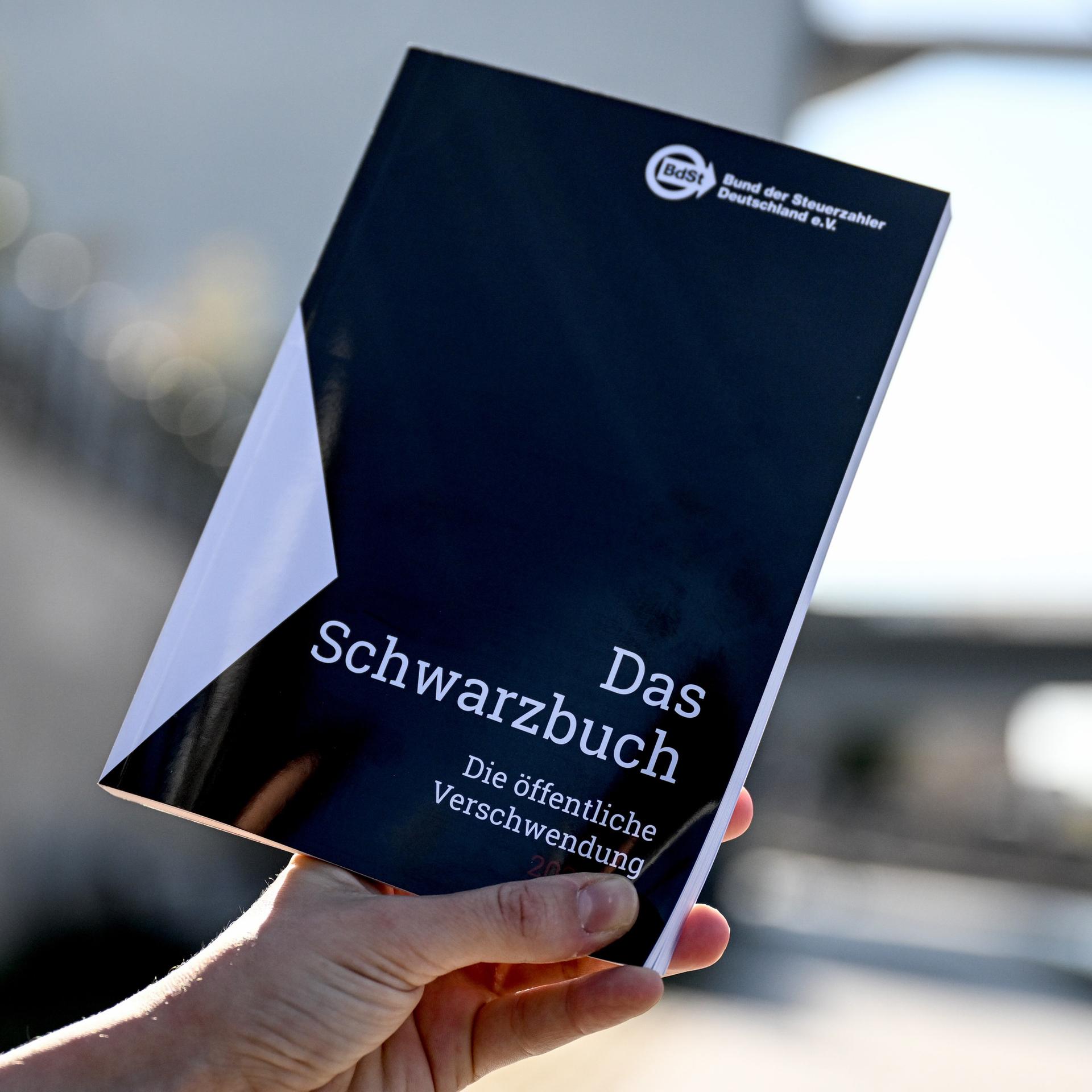 Das Schwarzbuch 2025/26 vom Bund der Steuerzahler wird von einer Hand gehalten. Das Schwarzbuch listet Beispiele auf, wo aus Sicht des Steuerzahlerbunds Steuergelder verschwendet wurden.