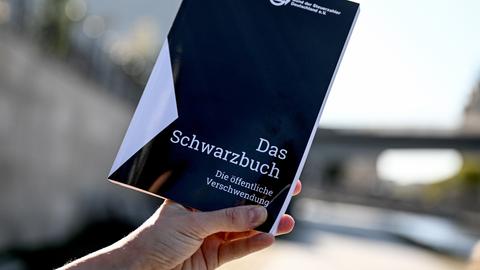 Das Schwarzbuch 2025/26 vom Bund der Steuerzahler wird von einer Hand gehalten. Das Schwarzbuch listet Beispiele auf, wo aus Sicht des Steuerzahlerbunds Steuergelder verschwendet wurden.