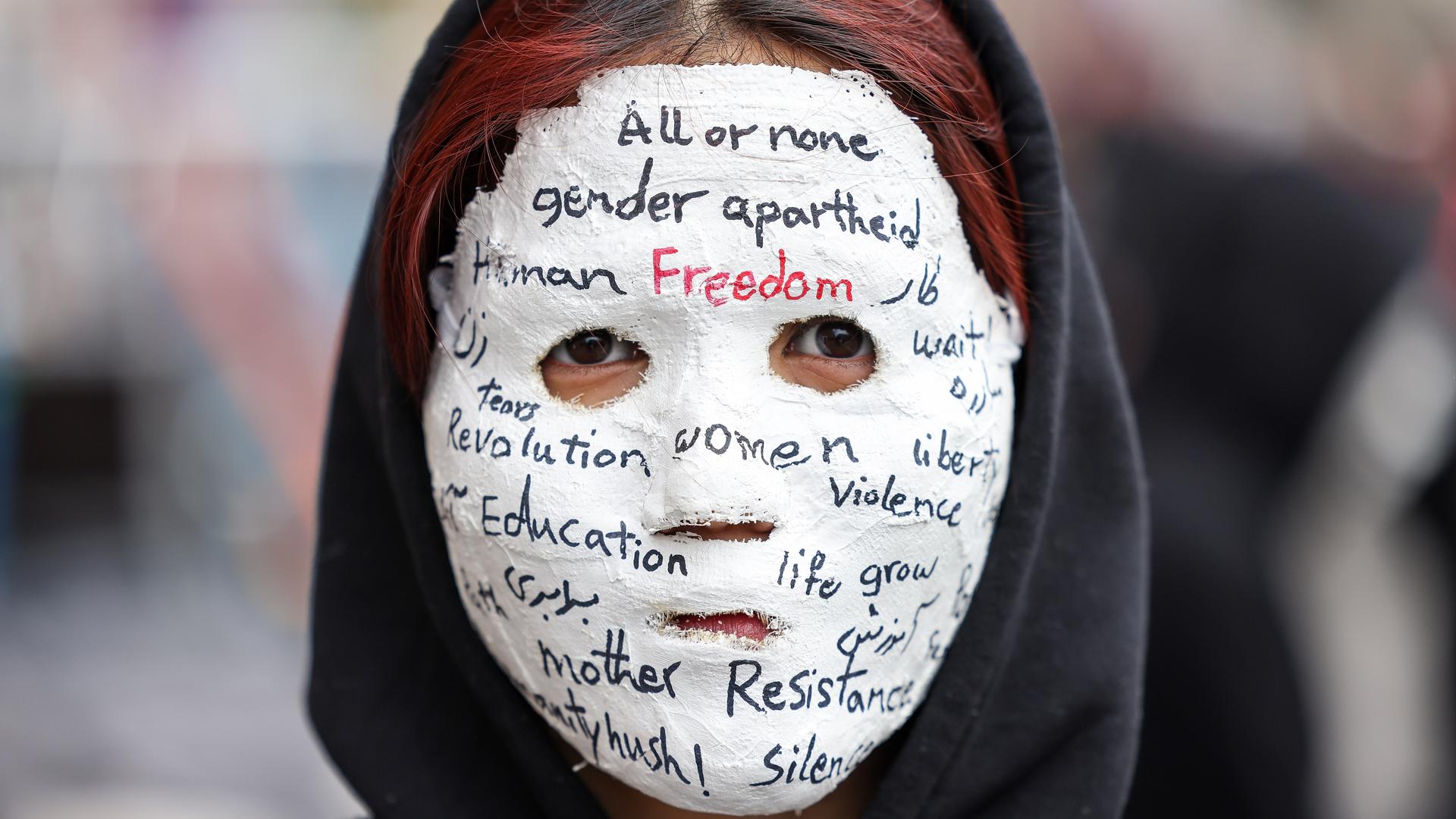 Eine Frau trägt eine Gipsmaske, auf der unter anderem steht: "All or none. Gender Arpartheid. Freedom. Eduaction. Resistance" 