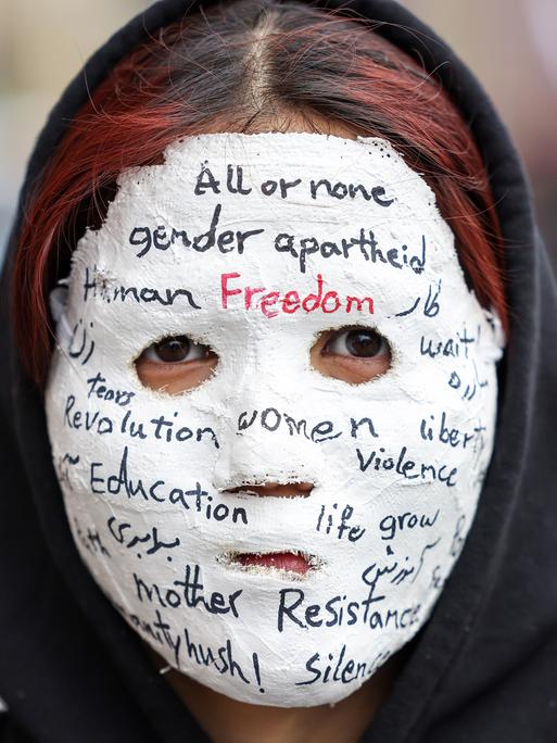 Eine Frau trägt eine Gipsmaske, auf der unter anderem steht: "All or none. Gender Arpartheid. Freedom. Eduaction. Resistance" 