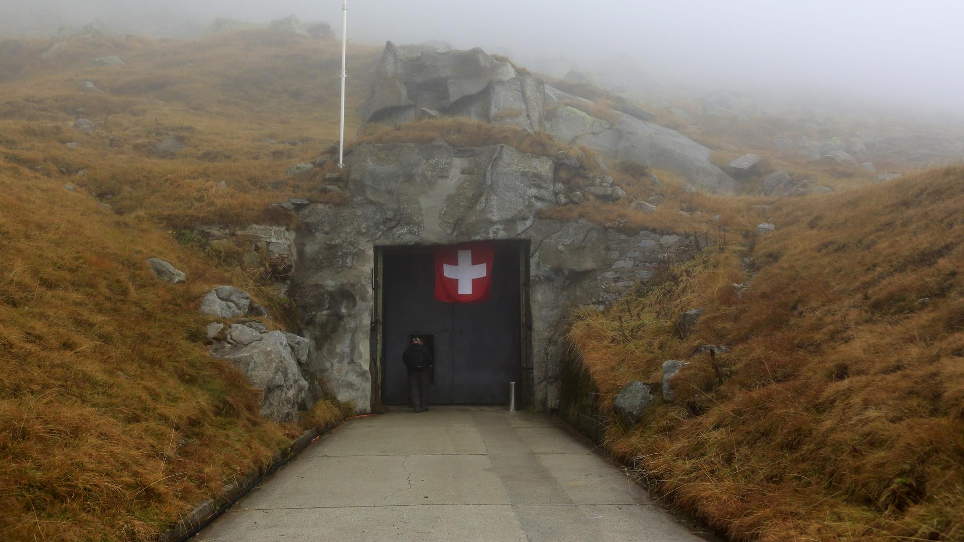 Blick auf den Eingang eines Bunkers, an dem eine schweizer Flagge hängt.