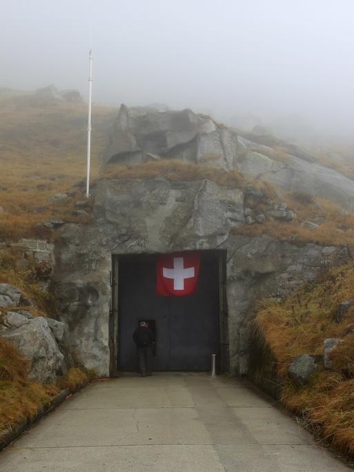 Blick auf den Eingang eines Bunkers, an dem eine schweizer Flagge hängt.
