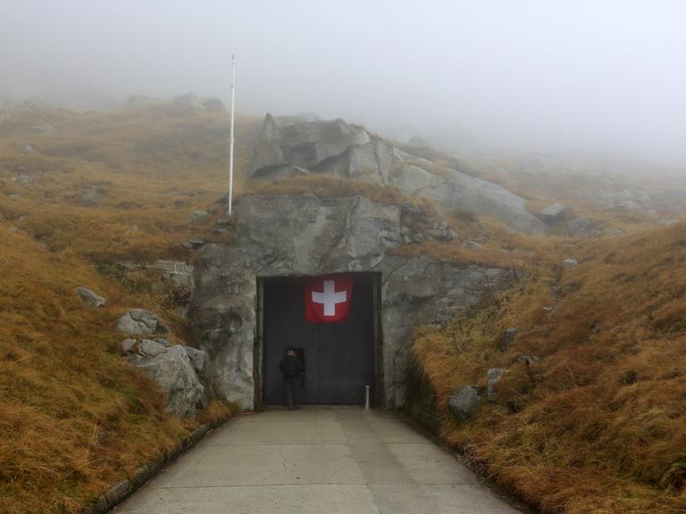 Blick auf den Eingang eines Bunkers, an dem eine schweizer Flagge hängt.