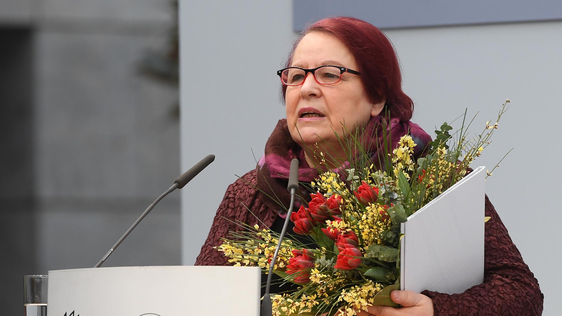 Eine Frau mit einem Blumenstrauss im Arm steht an einem Rednerpult