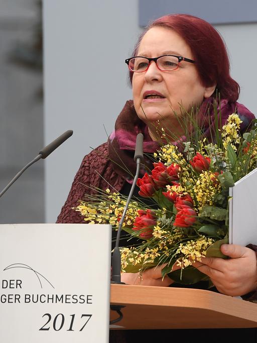 Eine Frau mit einem Blumenstrauss im Arm steht an einem Rednerpult