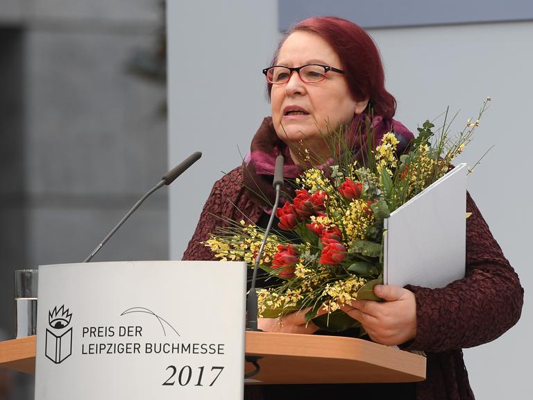 Eine Frau mit einem Blumenstrauss im Arm steht an einem Rednerpult