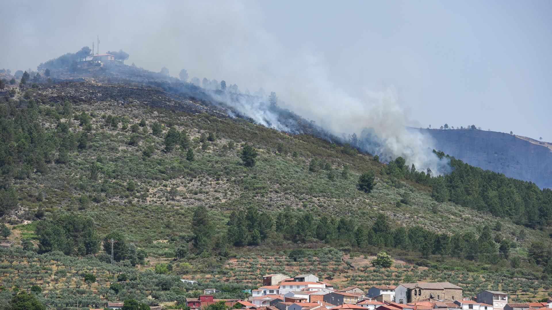 Wälder und Büsche brennen auf einem Berghang in der Nähe eines Dorfes.