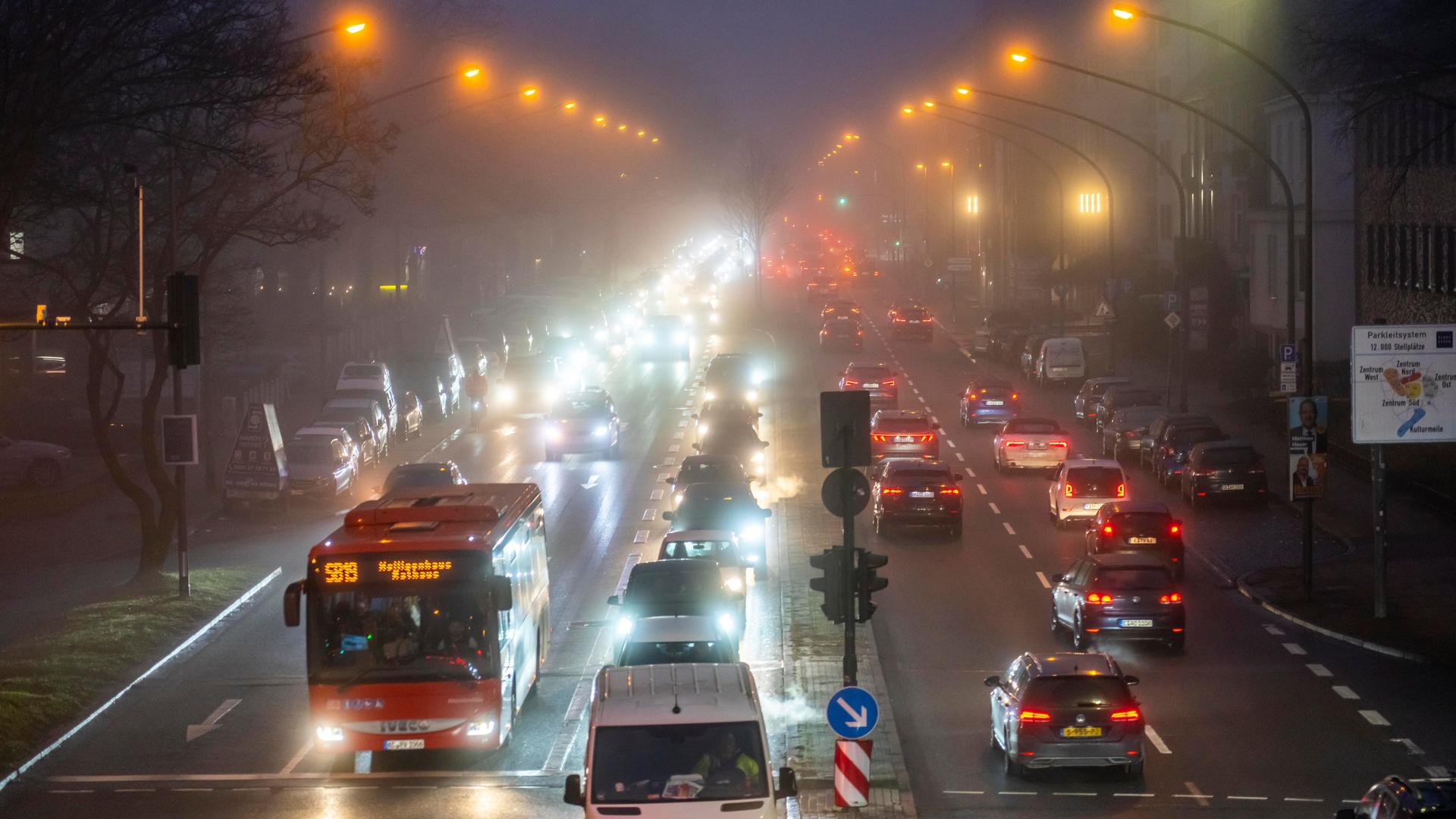 Dichter Verkehr auf einer innerstädtischen nächtlichen Straße im Nebel.