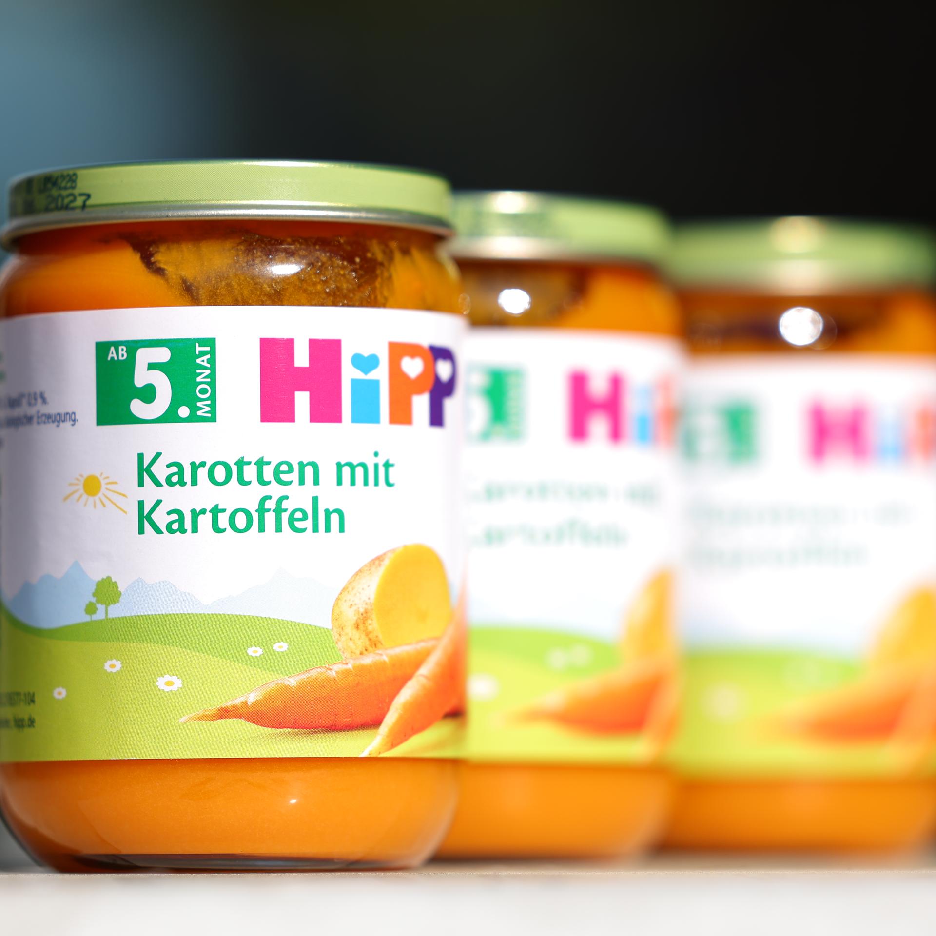 Auf einem Tisch stehen drei Artikel von der Sorte "Gemüsegläschen Karotte mit Kartoffel" des Herstellers Hipp.