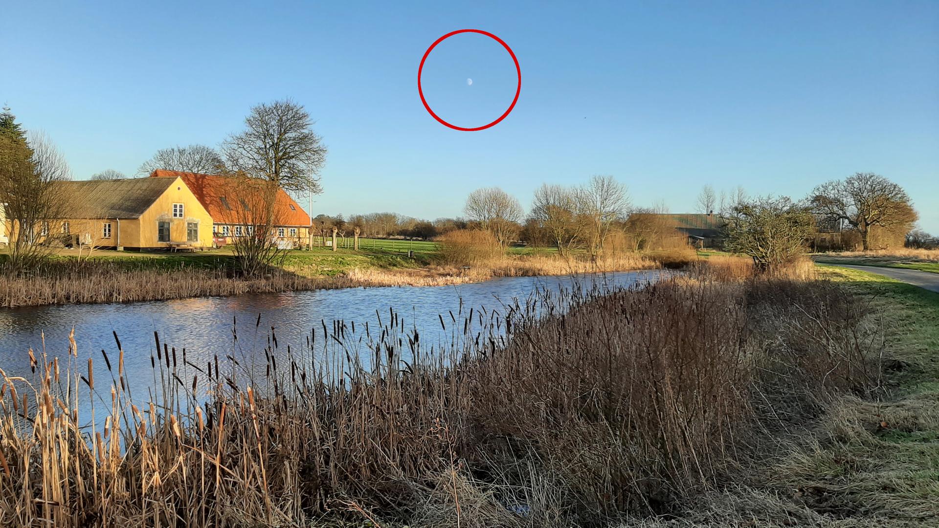 Am frühen Morgen steht der Mond über einem Haus an einem Fluss.