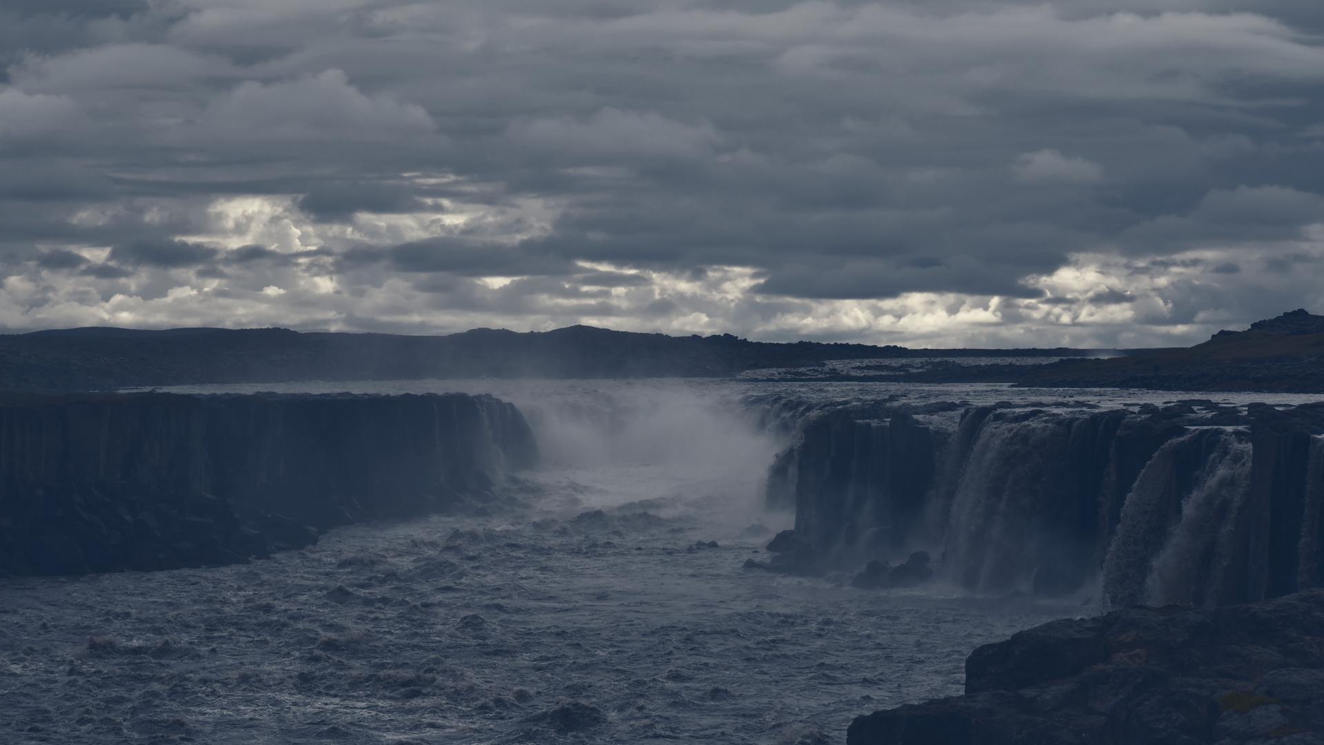 Der Wasserfall Hafragilsfoss in Gischt und Nebel, aufgenommen im August 2021. Darüber bricht die Sonne ganz leicht durch die Wolken.