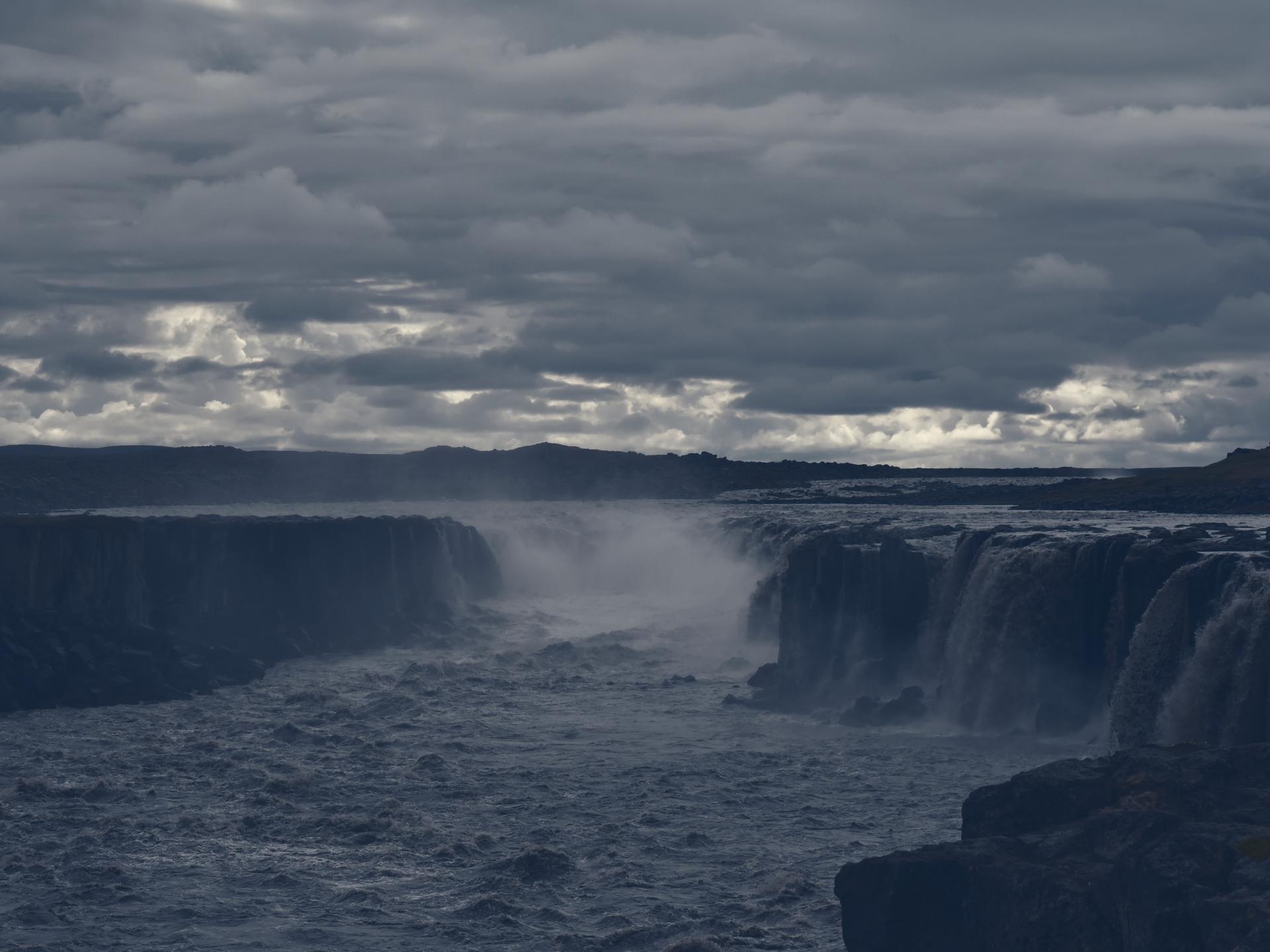 Der Wasserfall Hafragilsfoss in Gischt und Nebel, aufgenommen im August 2021. Darüber bricht die Sonne ganz leicht durch die Wolken.