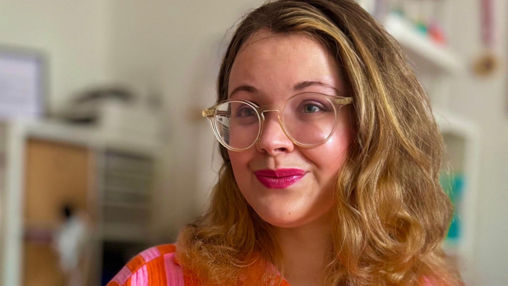 Tanya Yael Raab trägt eine rosaorange farbene Bluse und hält ihr Buch "Shalom zusammen!" im Arm. Tanya Yael Raab trägt eine rosaorange farbene Bluse und hält ihr Buch "Shalom zusammen!" im Arm.