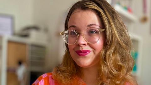 Tanya Yael Raab trägt eine rosaorange farbene Bluse und hält ihr Buch "Shalom zusammen!" im Arm.