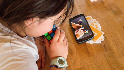 Ein Kind lernt mit Hilfe des Smartphones, wie man mit dem Zauberwürfel spielt 