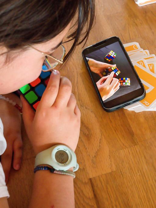 Ein Kind lernt mit Hilfe des Smartphones, wie man mit dem Zauberwürfel spielt 