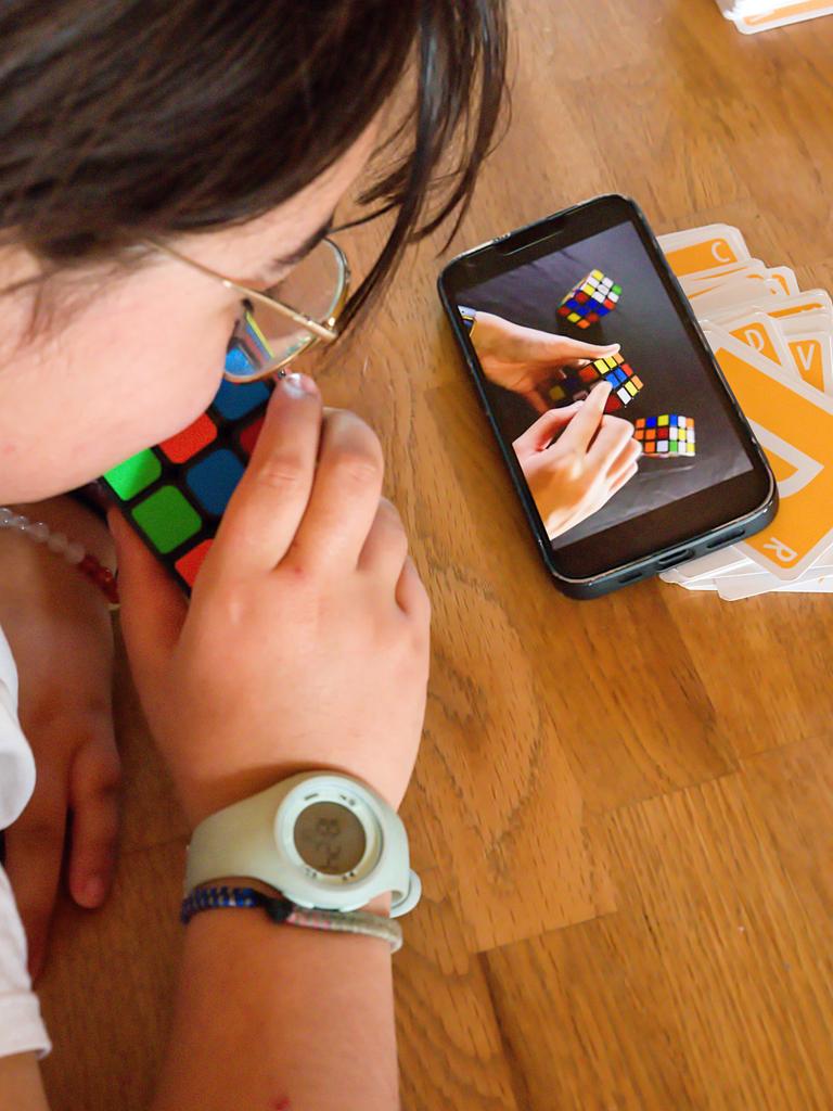 Ein Kind lernt mit Hilfe des Smartphones, wie man mit dem Zauberwürfel spielt 