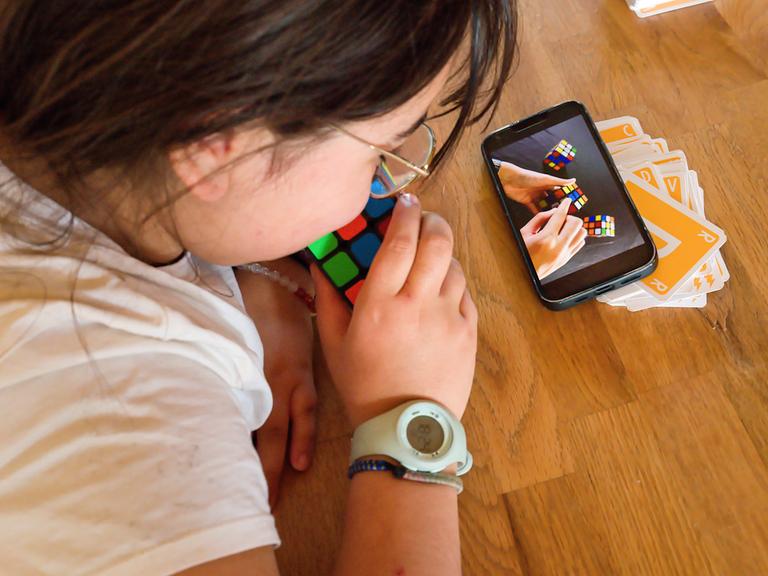 Ein Kind lernt mit Hilfe des Smartphones, wie man mit dem Zauberwürfel spielt 