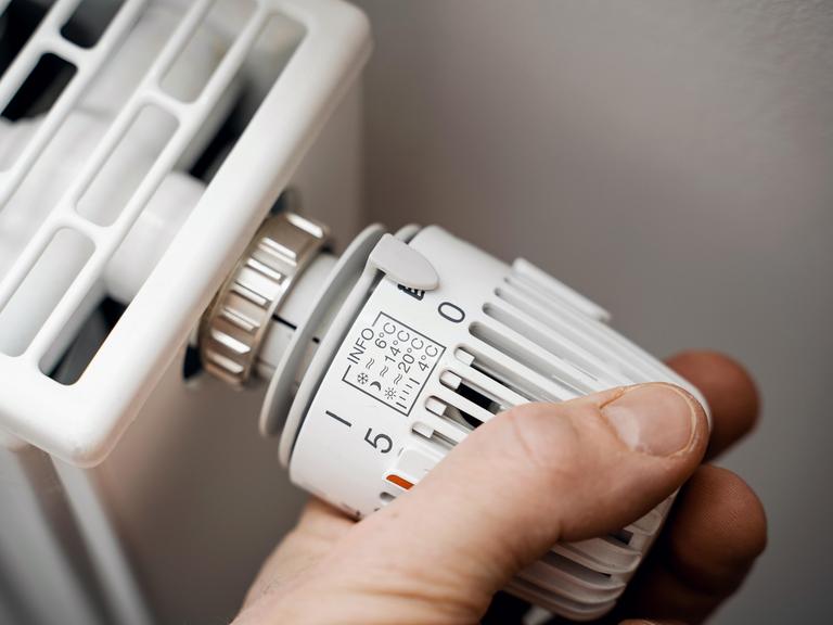 Eine Hand dreht den Thermostat einer Heizung auf Null.