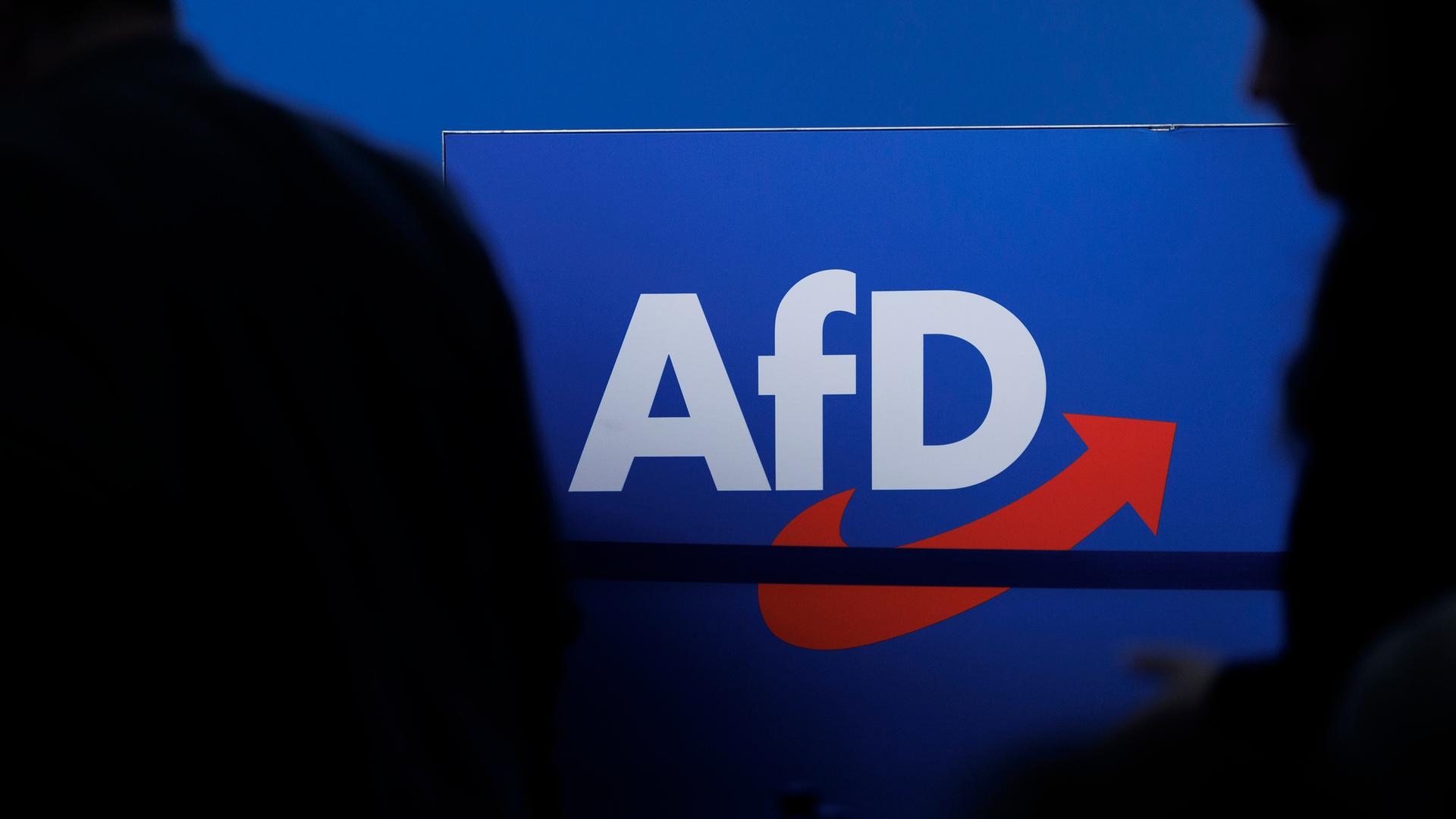 Das Parteilogo der AfD. Daneben sind die Schatten von mehreren Personen zu sehen. Das Parteilogo der AfD. Daneben sind die Schatten von mehreren Personen zu sehen.
