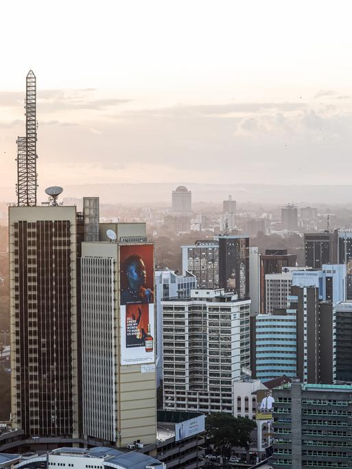 Zu sehen ist eine Luftaufnahme von Nairobi. Im Vorder- sowie im Hintergrund stehen mehrere Hochhäuser. Dazwischen schlängelt sich eine Straße.