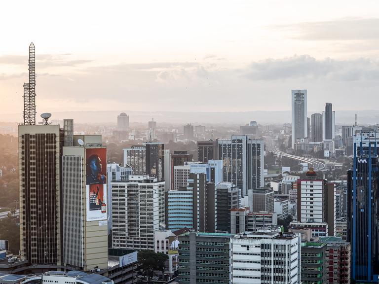 Zu sehen ist eine Luftaufnahme von Nairobi. Im Vorder- sowie im Hintergrund stehen mehrere Hochhäuser. Dazwischen schlängelt sich eine Straße.