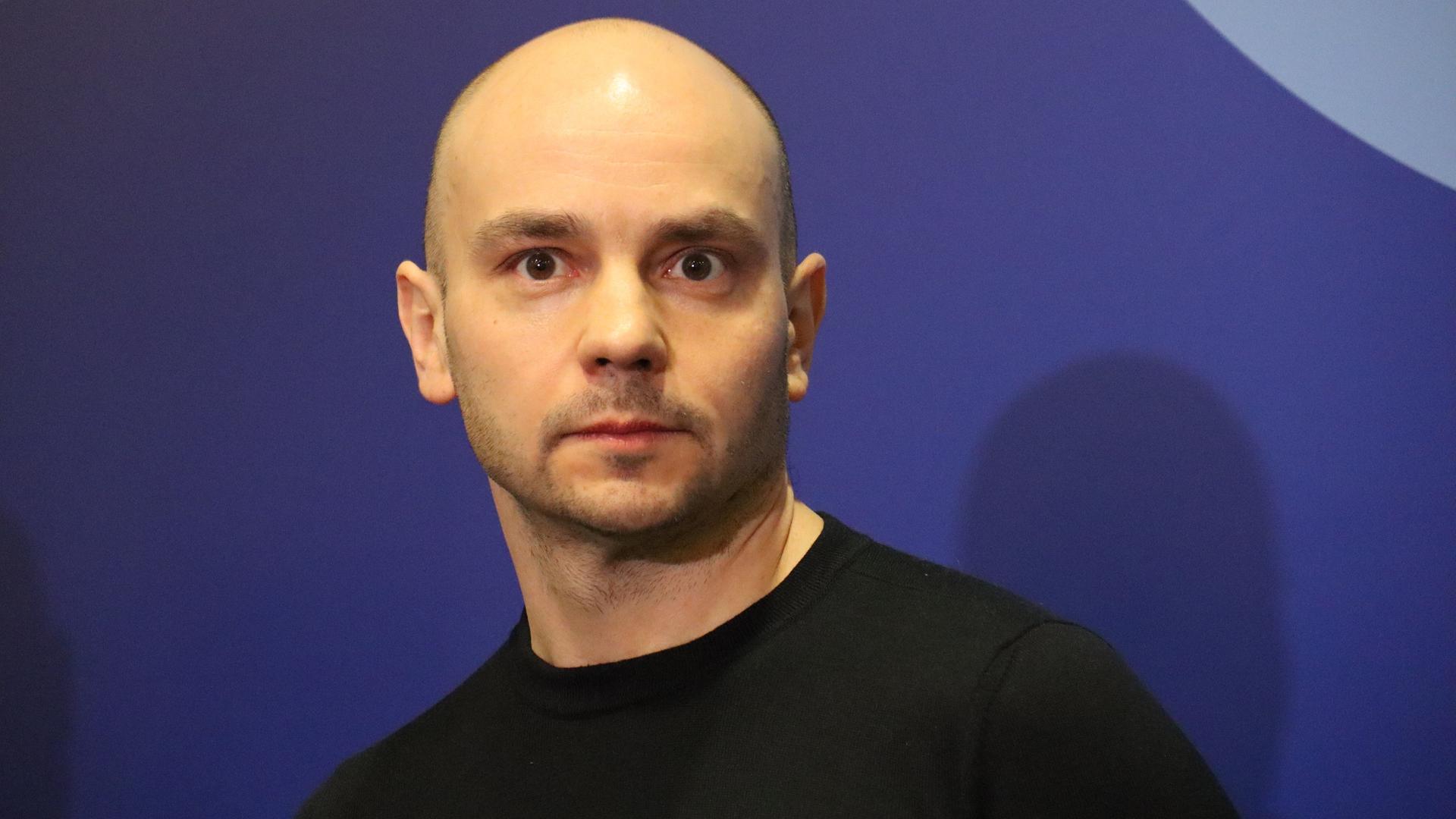 Andrej Pivovarow steht im Jahr 2021 bei einer Versammlung der russischen Opposition in Moskau mit einem schwarzen T-Shirt vor einem blauen Hintergrund.