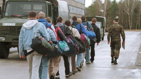 Junge Männer gehen angeführt von einem Soldaten in Tarnanzug an Militärfahrzeugen vorbei.