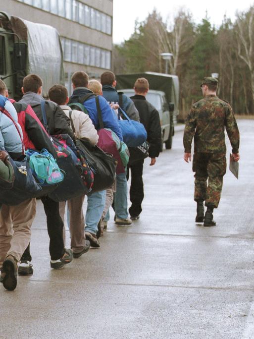 Junge Männer gehen angeführt von einem Soldaten in Tarnanzug an Militärfahrzeugen vorbei.