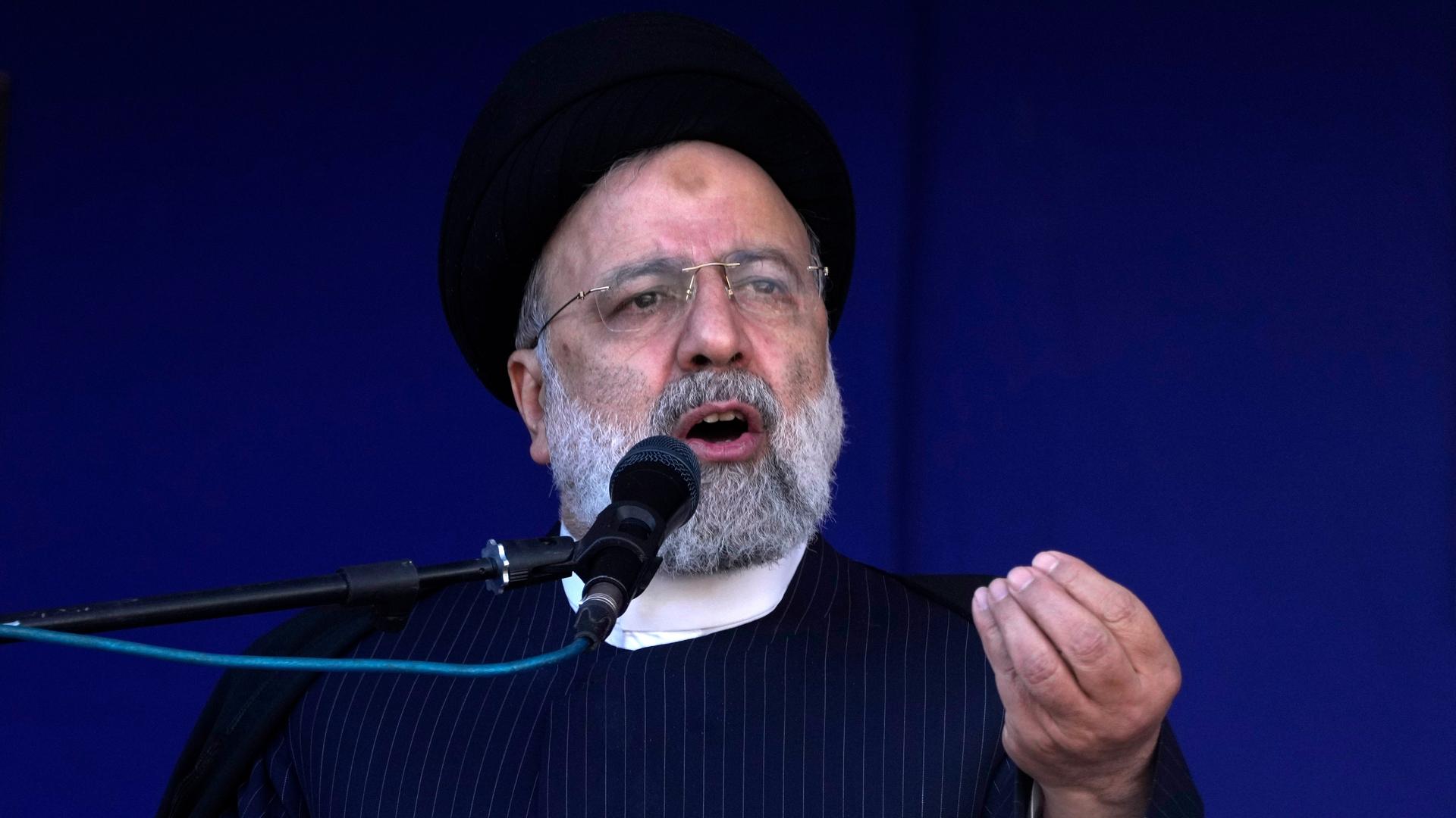Der iranische Präsident Raisi steht vor einem Mikrofon und gestikuliert.