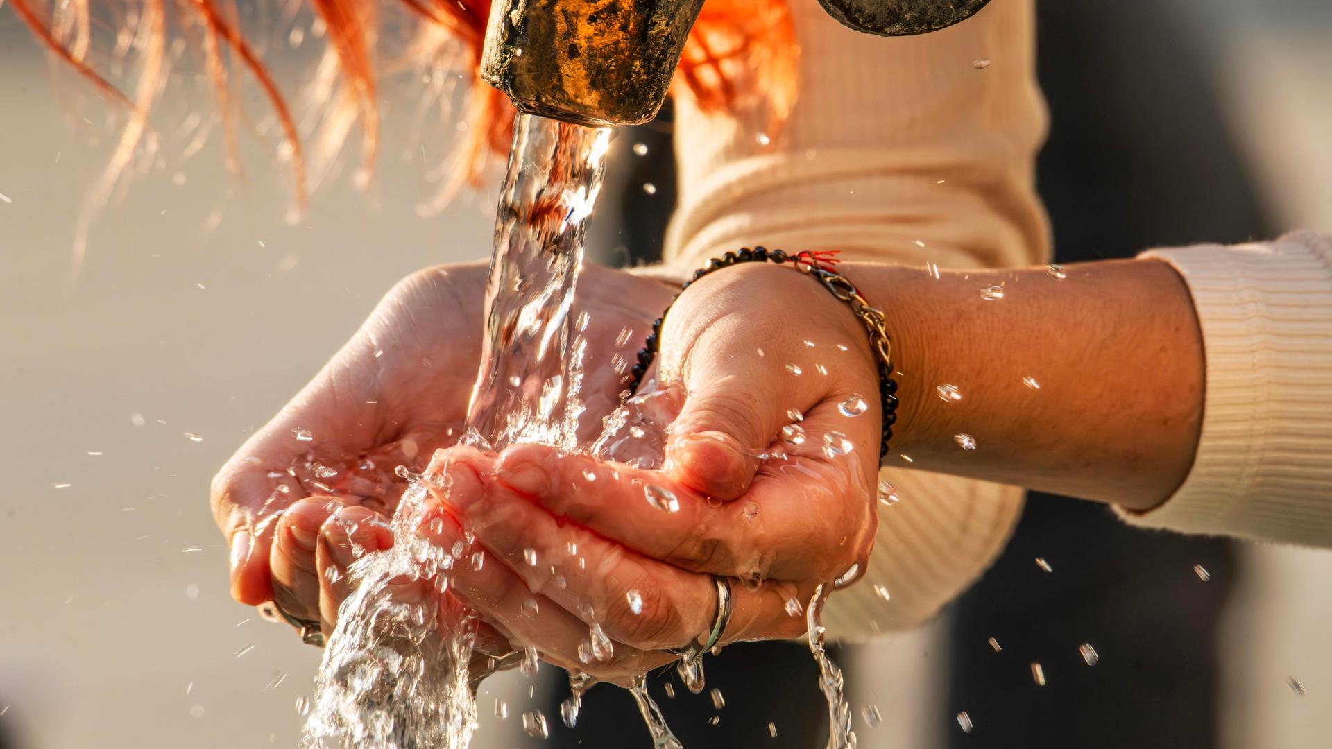 Eine Frau schöpft mit ihren Händen Trinkwasser aus einem Trinkwasserbrunnen.
