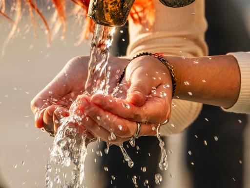 Eine Frau schöpft mit ihren Händen Trinkwasser aus einem Trinkwasserbrunnen.