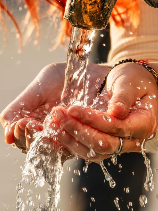 Eine Frau schöpft mit ihren Händen Trinkwasser aus einem Trinkwasserbrunnen. Eine Frau schöpft mit ihren Händen Trinkwasser aus einem Trinkwasserbrunnen.