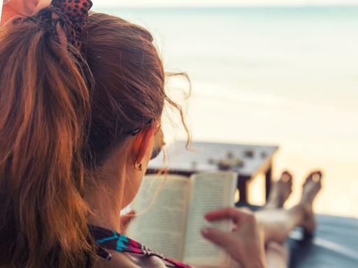 Eine junge Frau liest ein Buch am Strand.