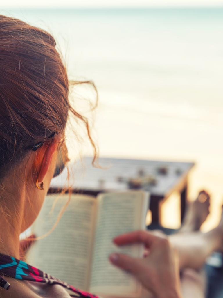 Eine junge Frau liest ein Buch am Strand.