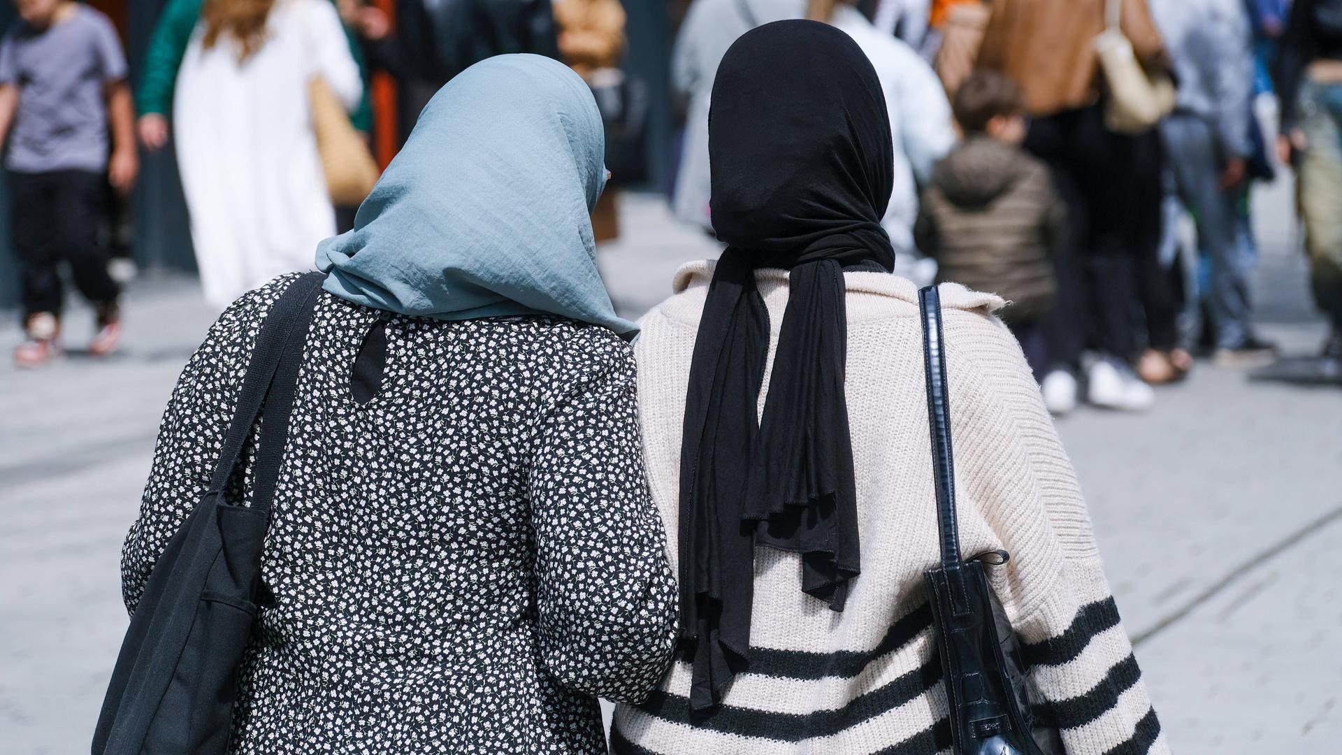 Zwei muslimische Frauen mit Kopftuch gehen in Düsseldorf auf der Straße Arm in Arm.
